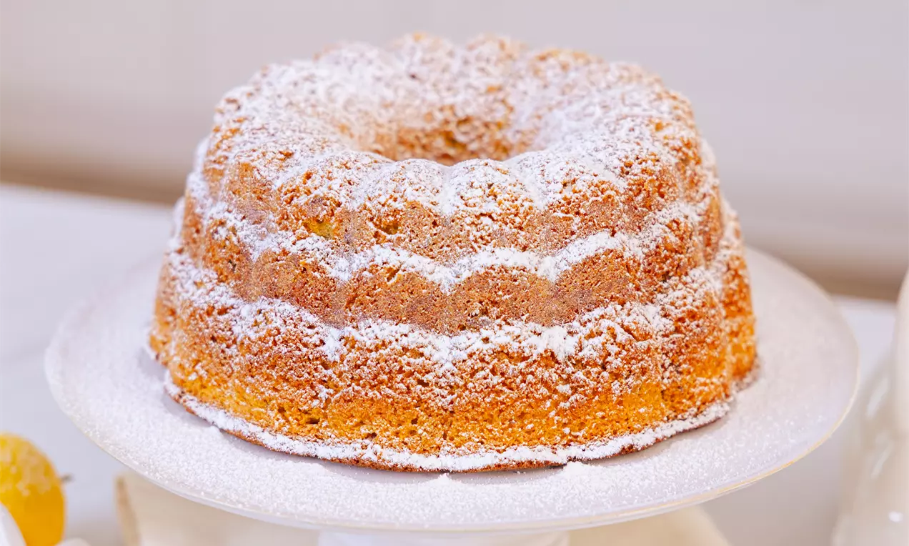 Zlato rjav orehov šarkelj z rebrasto obliko, posut z belim sladkorjem v prahu, na belem podstavku, obdan s limono in nežno svetlo dekoracijo